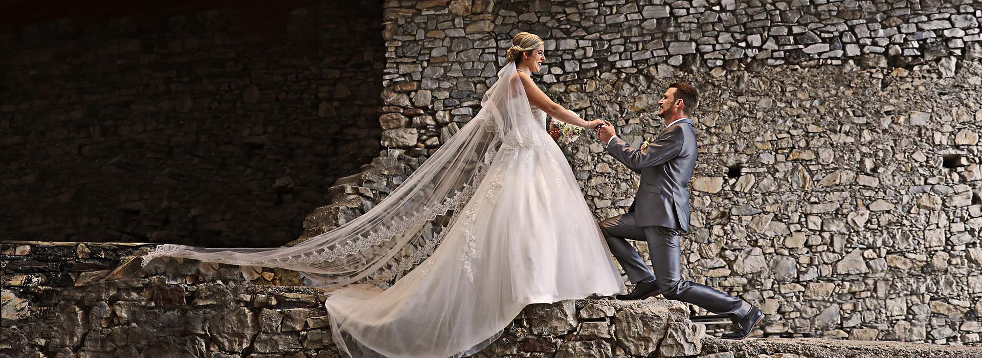 Braut mit Schleier und Bräutigam in Pose vor Burgmauern